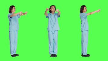 Asian nurse giving thumbs down in studio, showing dislike and negativity symbol over full body greenscreen backdrop. Displeased medical assistant expressing disagreement and disapproval. video