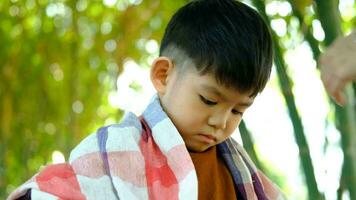 Barber cutting hair of an Asian boy In an open space filled with trees. video