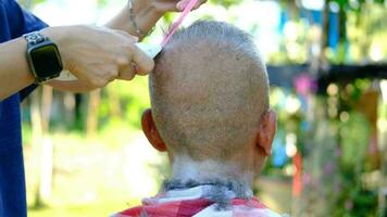 ett äldre asiatisk person får hans hår skära utomhus. video