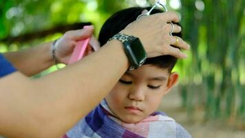 Barber cutting hair of an Asian boy In an open space filled with trees. video