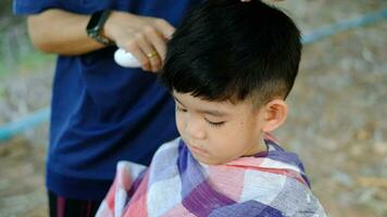 Barber cutting hair of an Asian boy In an open space filled with trees. video