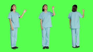 asiatico medico infermiera controlli ologramma nel studio con schermo verde disegno, Lavorando con olografico icona linguetta e artificiale intelligenza. maschio specialista nel uniforme con assistenza sanitaria competenza. video