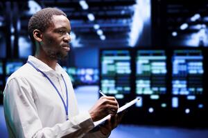 Experienced IT admin evaluating server rigs using renewable sources to reduce electronics carbon footprint. Engineer checking contingency plan on clipboard in sustainable high tech facility photo