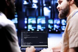 Colleagues updating server clusters, writing complex binary code scripts on laptop terminal. Admins using JavaScript, Java, and database programming to fortify security and safeguard data photo