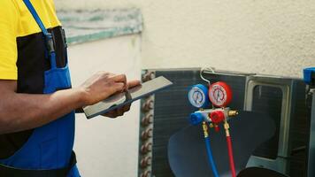 Certified technician doing hvac system inspection of freon levels and necessary fixes to prevent major breakdowns. Competent mechanic troubleshooting air conditioner, writing findings on clipboard photo