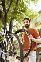 Enthusiastic young caucasian man carrying bicycle wheel to reattach and secure for summer leisure cycling. Image showing portrait of male cyclist with bike tire outdoor for yearly maintenance. photo
