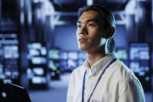 Certified technician in data center uses laptop to prevent system overload during peak traffic periods. Proficient employee in server room ensuring enough network bandwidth for smooth operations photo