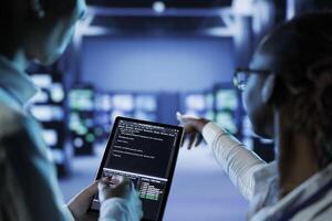 Qualified technicians building firewall systems in server room housing advanced infrastructure. Certified experts running code on tablet to upgrade data center rigs handling demanding workloads photo