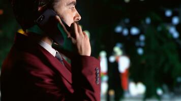 Stylish man answers phone call on night time walk, strolling around city center under streetlights. Business person chatting and walking, admiring urban landscape. Handheld shot. Close up. photo