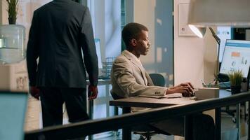 African american employee crosschecking financial figures between clipboard charts and diagrams on computer screen during nightshift. Efficient worker comparing company numbers in office photo