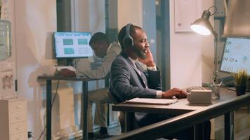 africano americano trabajador disfrutando música a tomar su mente lejos desde aburrido rutina proyecto Tareas durante Turno nocturno. empresario en oficina con auriculares en comparando márketing gráficos y estadísticas foto