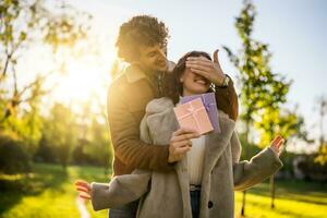 Portrait of happy loving couple in park in sunset. Man is giving present to his woman. photo