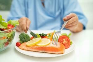 Asian elderly woman patient eating salmon steak breakfast with vegetable healthy food in hospital. photo