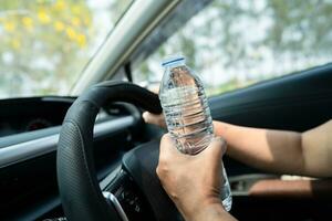 conductora asiática sosteniendo una botella para beber agua mientras conduce un automóvil. una botella de agua caliente de plástico provoca un incendio. foto