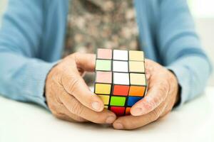 Bangkok, Thailand August 14, 2023 Alzheimer disease AD, Asian elderly woman patient playing Rubik cube game to practice brain training for dementia prevention. photo