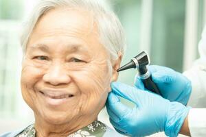 Audiologist or ENT doctor use otoscope checking ear of asian senior woman patient treating hearing loss problem. photo