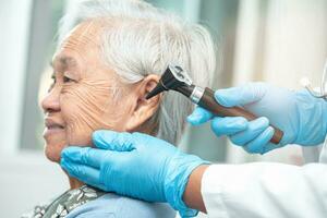 Audiologist or ENT doctor use otoscope checking ear of asian senior woman patient treating hearing loss problem. photo