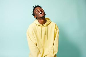 black guy smiling wearing yellow long sleeve shirt on blue background photo