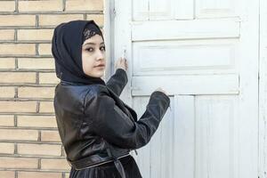 Portrait of beautiful middle-eastern girl in traditional Islamic clothing - hijab. Modern and young Iranian woman in leather jacket photo