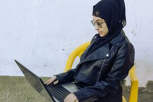 hermosa Medio este trabajando con el ordenador portátil. linda árabe musulmán mujer en hijab posando con ordenador portátil al aire libre. bloguero, vloguero, persona de libre dedicación niña a el trabajo proceso foto