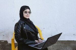 Beautiful middle-eastern working with the laptop. Cute Arabian Muslim woman in hijab posing with laptop outdoors. Blogger, vlogger, freelancer girl at the job process photo