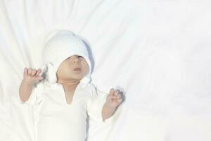 Curious little baby boy wearing white knitted hat and lying on white photo