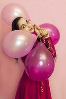 Young pretty woman in red evening dress holding festive air balloons. Portrait of happy 20s middle-eastern female celebrating valentines day, birthday, party photo