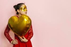 Woman wearing masquerade mask and holding heart shaped air ballon. Valentines Day, Birthday, Anniversary, Festive, Ball celebration concepts photo