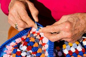 an older woman is knitting a colorful crochet blanket photo