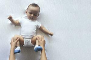 bebé masaje. mamá haciendo gimnasia con niño. mamá masajear linda bebé chico. Moviente del bebe piernas a ayuda aliviar constipación. joven madre haciendo ejercicios y movimientos a estimular del bebe intestinos. foto