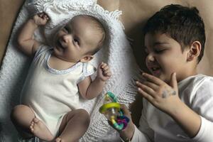 dos hermanos acostado y posando retrato de hermanos dos meses bebé chico y cinco años pequeño chico jugando alegremente ver desde arriba. emocional expresiones de niños. foto