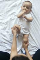 Baby massage. Mom doing gymnastics with kid. Mommy massaging cute baby boy. Moving baby's legs to help relieve constipation. Young mother doing exercises and movements to stimulate baby's bowels. photo