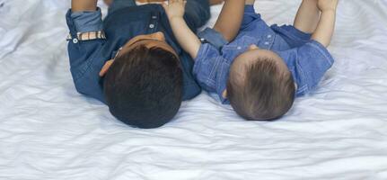 dos pequeño hermanos leyendo un libro. infantil niños acostado en el cama y leer el cuento antes de durmiendo. leyendo un corto historia para niños. medio oriental niños en su cama. foto