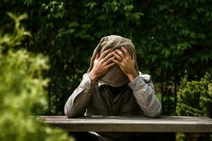 Man sitting on bench in garden and covering his face with hands, man in depression photo