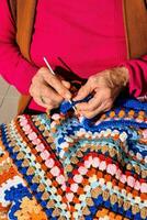 an older woman is knitting a colorful crochet blanket photo