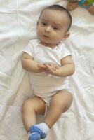 6-8-month-old baby boy lying playfully in bed. Charming 6-7 month little baby in white bodysuit. Baby boy in white bedding. Copy space photo