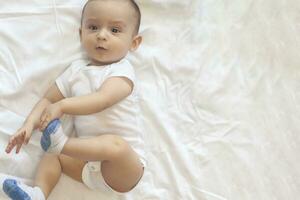 6-8-month-old baby boy lying playfully in bed. Charming 6-7 month little baby in white bodysuit. Baby boy in white bedding. Copy space photo