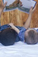 dos pequeño hermanos leyendo un libro. infantil niños acostado en el cama y leer el cuento antes de durmiendo. leyendo un corto historia para niños. medio oriental niños en su cama. foto