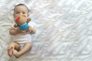 6-8-month-old baby boy lying playfully in bed. Charming 6-7 month little baby in white bodysuit. Baby boy in white bedding. Copy space photo