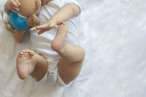 6-8-month-old baby boy lying playfully in bed. Charming 6-7 month little baby in white bodysuit. Baby boy in white bedding. Copy space photo