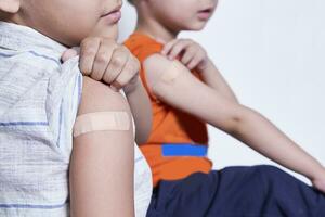 Two boys showing their arm with adhesive bandage plaster after vaccination. Injection covid vaccine, immunization for family photo