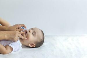 Little boy getting nasal drops. Pediatrician putting saline drops in infant's nose. Mother hands clearing the nose of baby. 6-month baby boy gets nose drops. photo