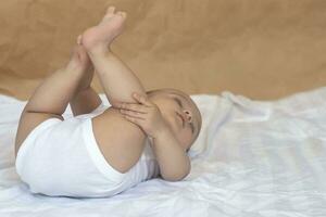 6-8-month-old baby boy lying playfully in bed. Charming 6-7 month little baby in white bodysuit. Baby boy in white bedding. Copy space photo