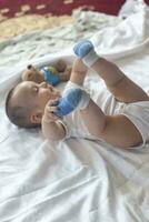 6-8-month-old baby boy lying playfully in bed. Charming 6-7 month little baby in white bodysuit. Baby boy in white bedding. Copy space photo