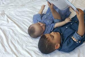 dos pequeño hermanos leyendo un libro. infantil niños acostado en el cama y leer el cuento antes de durmiendo. leyendo un corto historia para niños. medio oriental niños en su cama. foto
