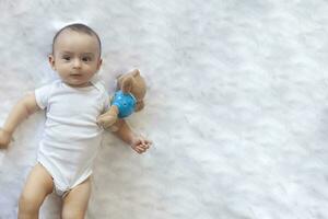 6-8-month-old baby boy lying playfully in bed. Charming 6-7 month little baby in white bodysuit. Baby boy in white bedding. Copy space photo