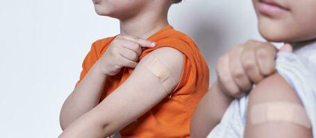 Two boys showing their arm with adhesive bandage plaster after vaccination. Injection covid vaccine, immunization for family photo