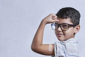 Portrait of happy healthy young kid showing bandage plaster on arm shoulder after getting vaccination photo