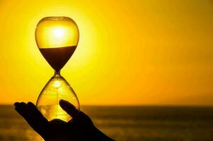 a person holding up a hourglass in front of the sunset photo