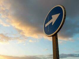 a blue and white sign with an arrow pointing in the direction of the road photo